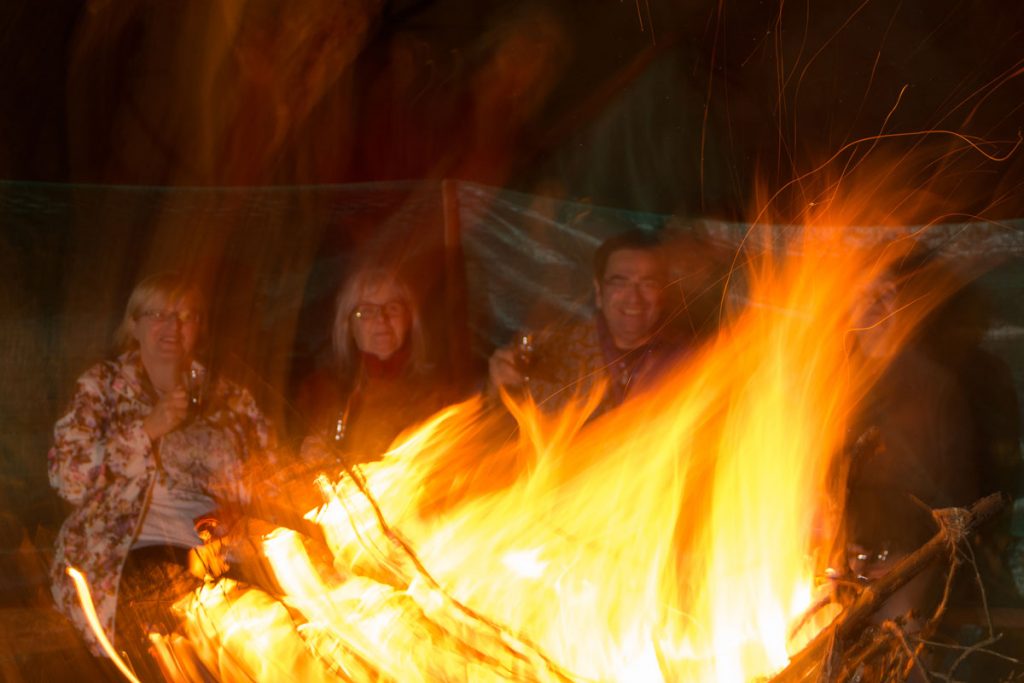Teilnehmer sitzen am Abend an einem lodernden Lagerfeuer